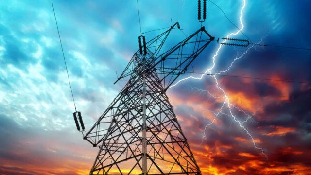 A transmission tower and power lines with lightning against a dramatic sky at sunset